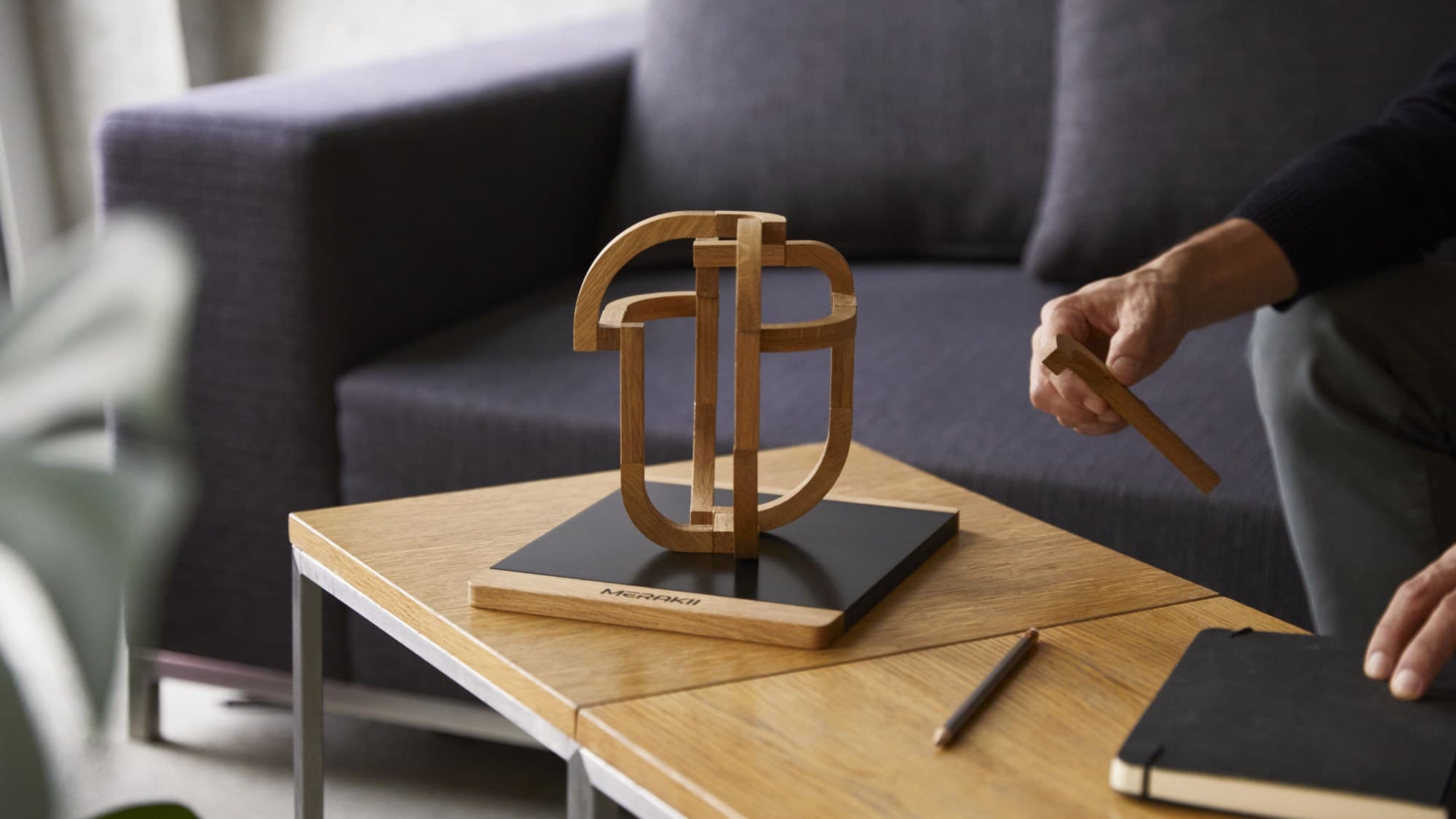Hands adding a curved wooden element to a MERAKII build in a living room